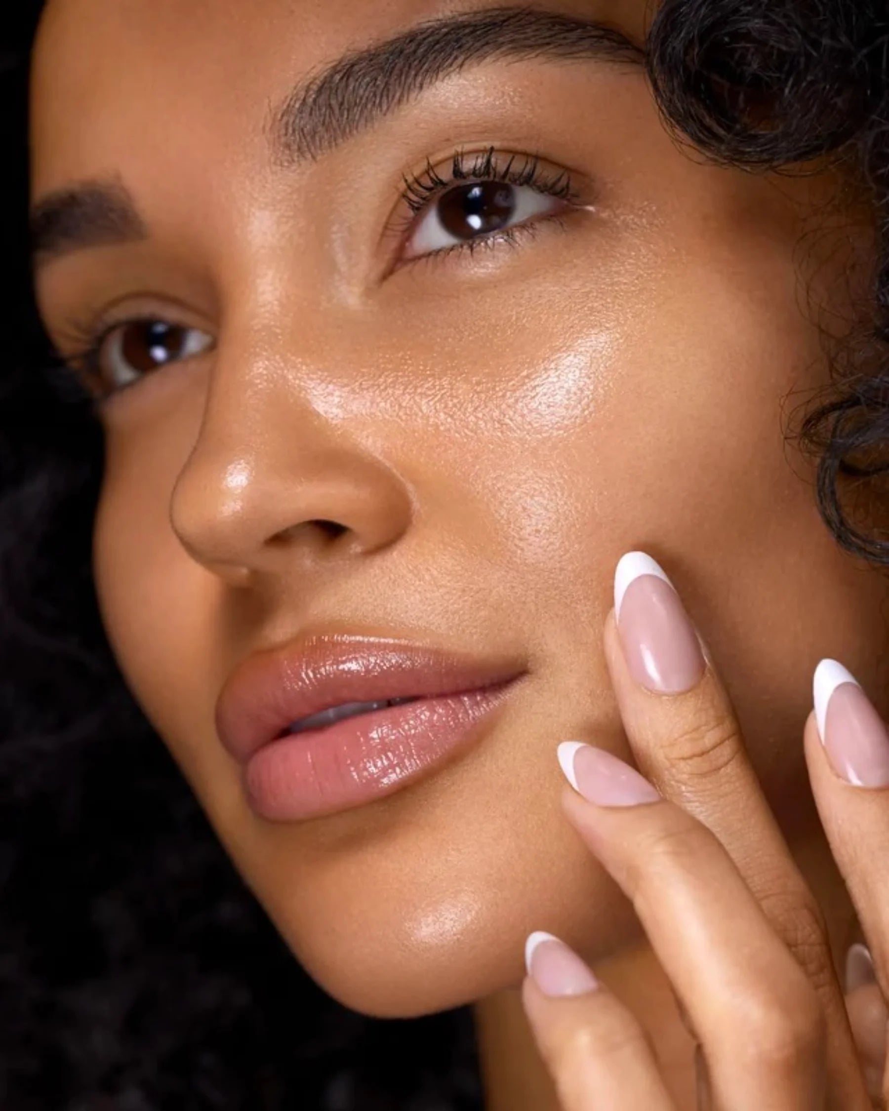 Close-up of woman with luminous skin touching her cheek for Filthy Rich Face Oil