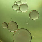 Macro view of golden green oil droplets representing Filthy Rich Reviving Face Oil texture