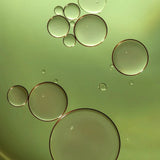 Macro view of golden green oil droplets representing Filthy Rich Reviving Face Oil texture