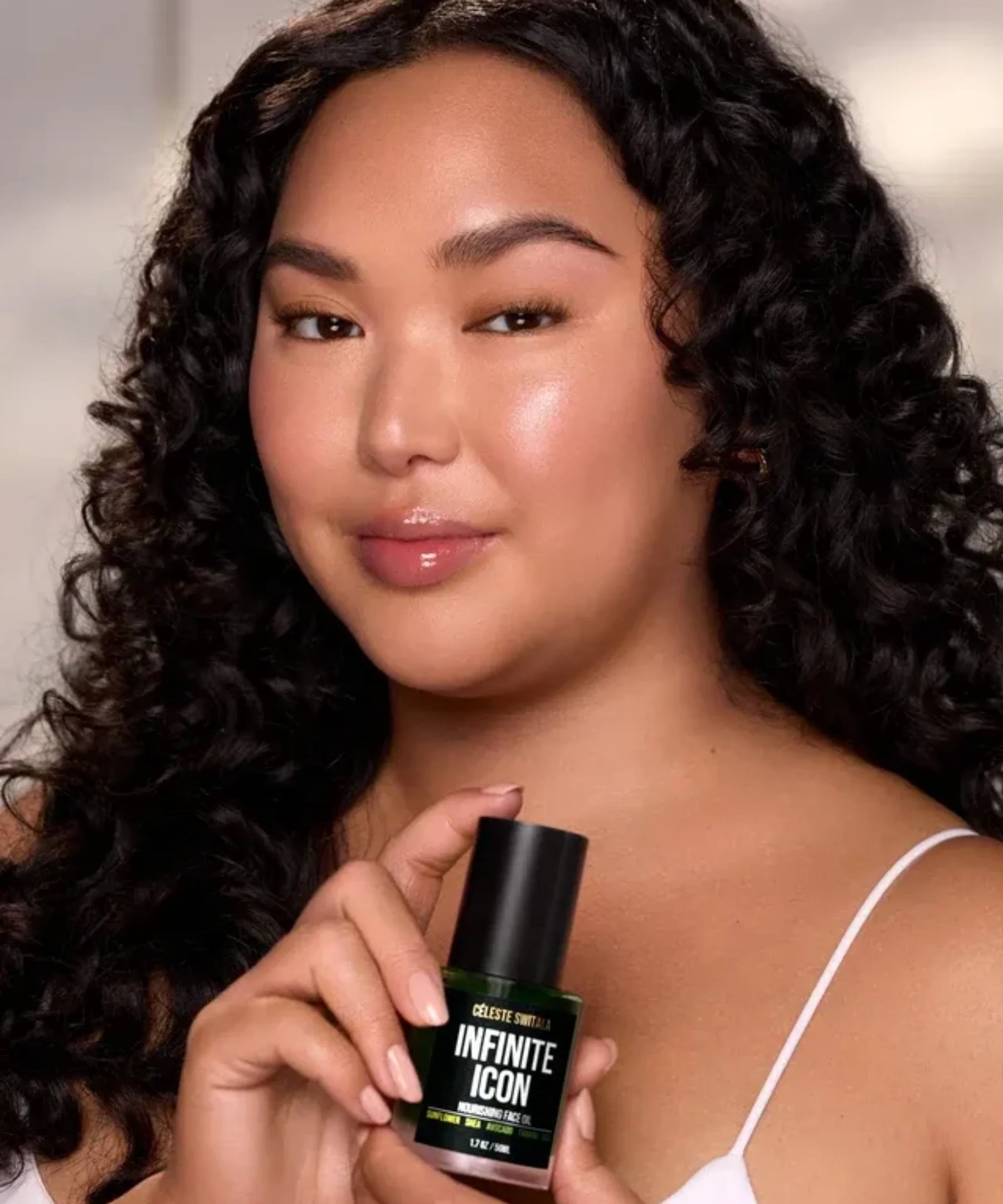 Woman holding Infinite Icon Nourishing Face Oil bottle with radiant and hydrated-looking skin